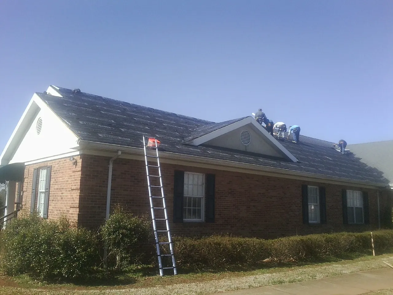 Crew tearing shingles off a brick ranch roof with a ladder set — Metal Roof Repair work by our crew in Floyd
