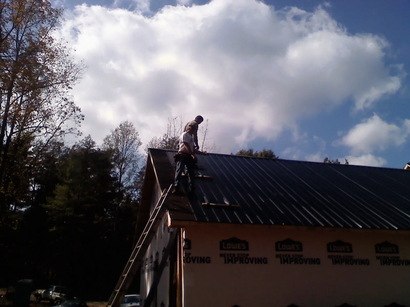 Roofer fastening dark metal panels high against a cloudy sky, from a Roof Inspection job in Floyd