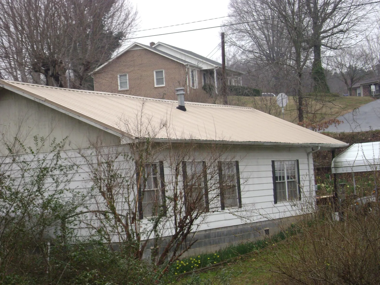Tan metal roof on a white sided house set into a hillside — Commercial Roofing by Roofing Brothers in Floyd
